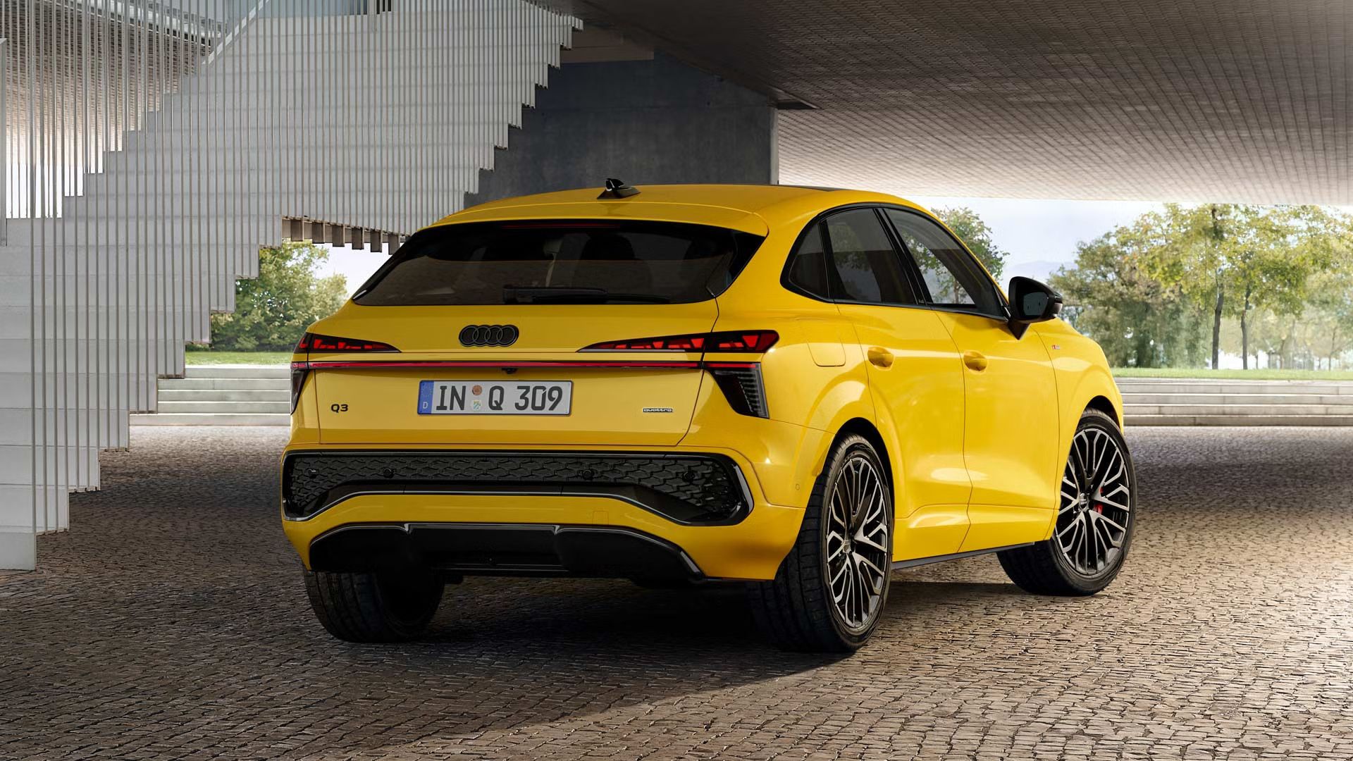 Ein gelber Q3 Sportback parkt auf gepflastertem Untergrund vor einem Treppengeländer.